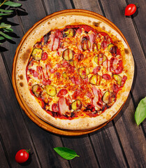 Delicious pizza topped with meats and pickles on a rustic wooden table