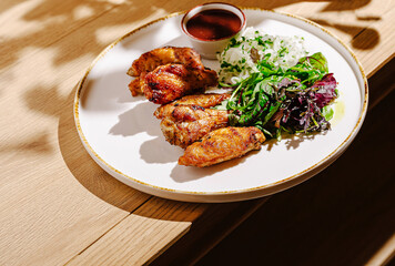 Delicious grilled chicken wings served with fresh salad on a wooden table