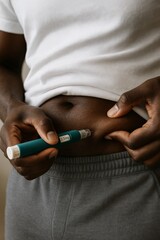 A young Black man self-injects GLP-1 medication into his belly using a injector pen. Semaglutide injection process