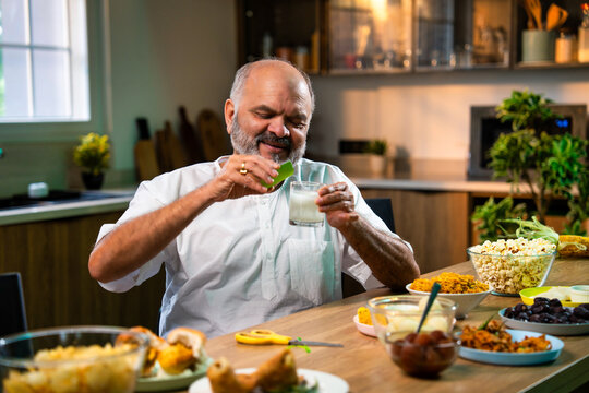 Elderly Indian man drinks antacid in modern kitchen after eating