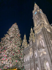 A christmas market with a large lit tree next to the city hall in vienna at night, concept of tourism, travel, holiday celebrations