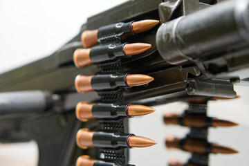 Belt of brass cartridges feeds into an automatic machine gun; copper tips and black links in sharp...