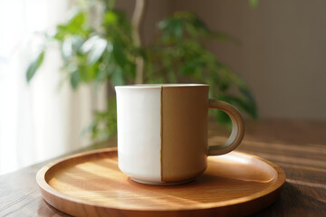 Obraz premium Cozy coffee mug with warm tones on wooden tray near sunny window