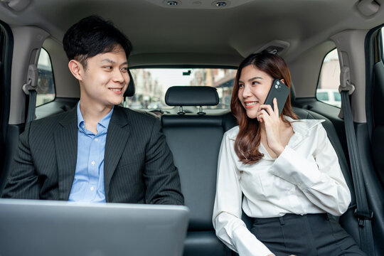Asian businessman and woman working while sitting in back seat of a car. - Powered by Adobe