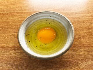 Fresh raw egg with golden yolk and clear egg white in ceramic bowl on wooden table, minimal style food photography highlighting natural texture, cooking ingredient and healthy protein source