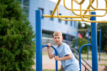 Obraz premium Blond boy hanging on monkey bars at outdoor playground
