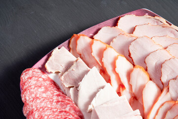 A plate of meat and cheese with a pinkish color. The meat is sliced and arranged in a way that it...
