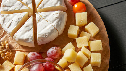 A wooden tray with a variety of cheese and fruit on it. The cheese is cut into pieces and the fruit is sliced. The tray is placed on a wooden table