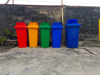 A row of five colorful waste bins against a concrete wall