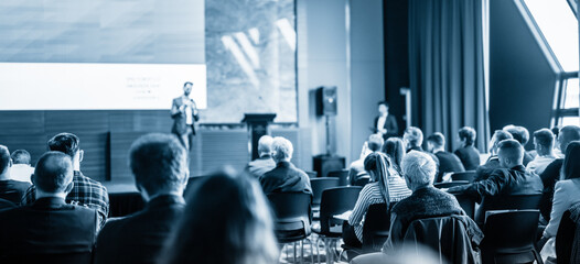 Speaker giving a talk in conference hall at business event. Blue toned black and white image