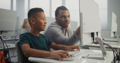 African American Smart Boy Using Computer, Doing Creative 3D Design Project. Teacher Helping Young Elementary School Student in Learning Coding During Digital Programming Lesson. Modern STEM Education