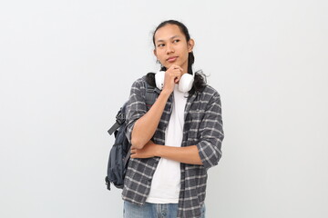 Young Asian male student wearing casual clothes and backpack, headphones around neck, thinking or...