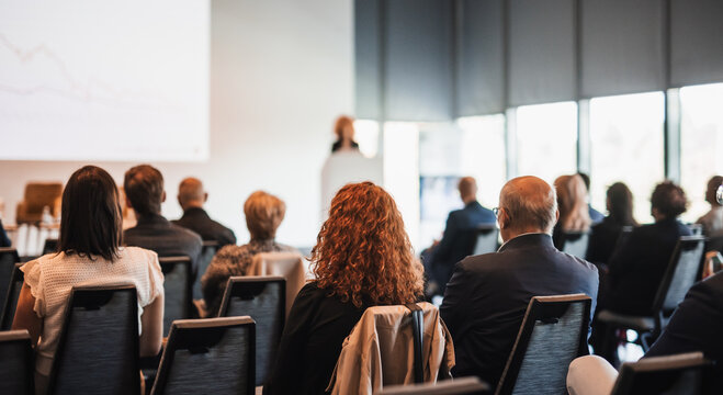 Female speaker giving a talk on corporate business conference. Unrecognizable people in audience at conference hall. Business and Entrepreneurship event