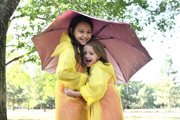 Happy girls, sisters are laughing and playing in the rain. Children enjoy a summer day