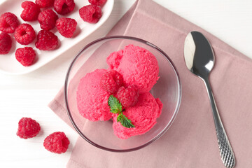 Delicious raspberry sorbet with mint in bowl, spoon and fresh berries on white wooden table, flat...