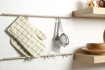 Oven glove, potholder and other kitchen utensils on metal rack indoors