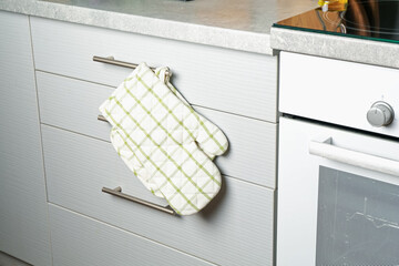 Oven glove and potholder hanging on handle of cabinet in kitchen