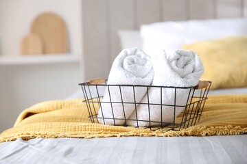 Clean towels in metal basket on bed linens at home, closeup