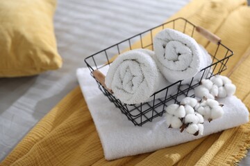 Clean towels, metal basket and cotton flowers on bed linens, closeup