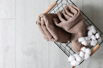 Clean towels and cotton flowers in metal basket on light wooden floor, top view. Space for text
