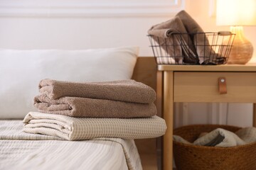 Stack of clean towels on bed linens and nightstand at home