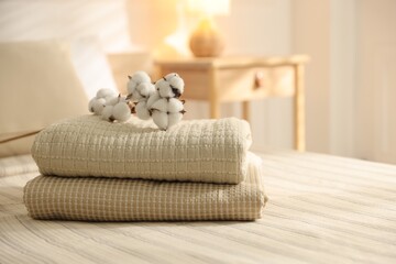 Stack of clean towels and cotton flowers on bed linens at home, closeup