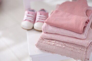 Stack of clean baby clothes and shoes on small chair indoors, closeup. Space for text