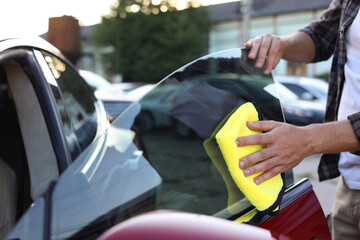 Man wiping car side window with yellow microfiber rag outdoors, closeup