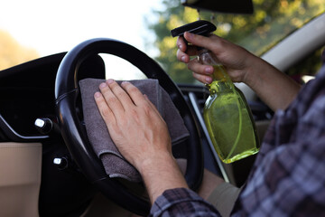 Man wiping steering wheel with grey microfiber rag in car salon, closeup