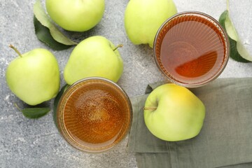 Delicious cider in glasses, apples and leaves on grey textured table, flat lay