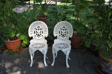 Deux chaises anciennes en fer forgé blanc dans un jardin.