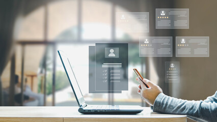 A person uses a smartphone to review digital candidate profiles and ratings on a holographic interface above a laptop in an office.