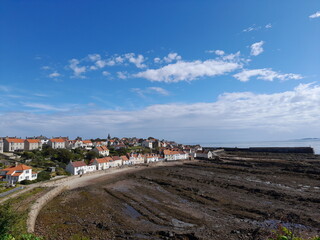 An above view of Pittenweem's coastline with the North Sea. The low tide reveals the rocky beach and forms rock pools filled with water reflecting the blue, clear sky. Taken in the East Neuk of Fife.