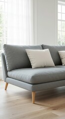 A light-gray sectional sofa with off-white cushions sits on a light-colored wooden floor in a bright, modern living room with sheer curtains.