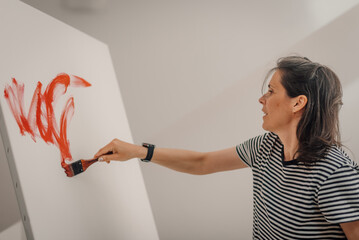 Female artist painting abstract red shapes on white canvas