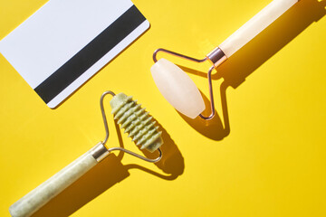 Dual jade and rose quartz facial rollers on vibrant yellow background.