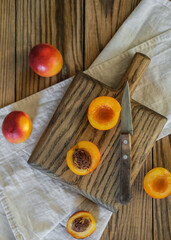 Fresh nectarines on rustic wooden table with two sliced halves on cutting board beside knife. Perfect for showcasing healthy summer recipes, natural food preparation or farmhouse kitchen aesthetic