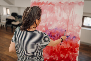 Female artist painting abstract modern art on large canvas in art studio