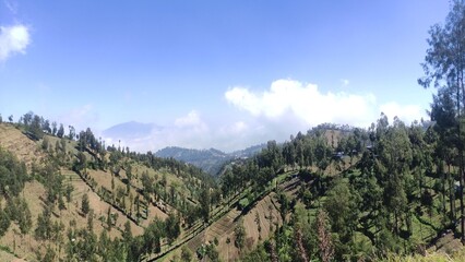 Beautiful mountain landscape with blue sky and clouds, showing natural hills and green trees. Perfect for travel blogs, tourism promotion, nature backgrounds, wallpapers, and educational materials.