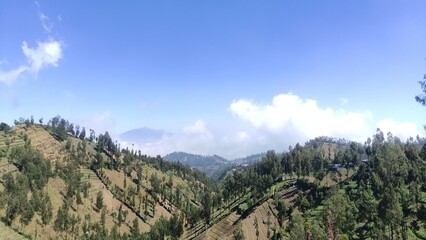 Naklejka premium Mountain view with clear blue sky and white clouds, showing natural hills and green forest. Perfect for travel blogs, tourism promotion, eco projects, backgrounds, and educational purposes.