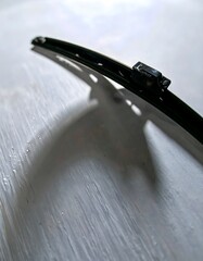 Close-up of a car windshield wiper blade casting a shadow on a textured surface