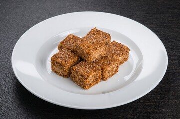 Cubes of sesame-crusted tofu on a white plate on a dark wood surface