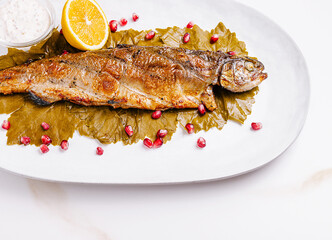 Grilled fish served on grape leaves with pomegranate seeds and lemon