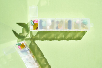 Vibrant pill organizer with shadow cast on light green background.