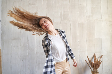 Happy caucasian young female tossing long hair in casual outfit with checkered shirt.