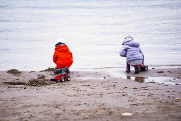 Children playing on a cold beach with toy tractor