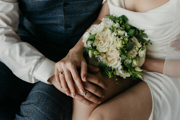 The bride and groom are sitting side by side, placing their hands on the bride's lap and showing...
