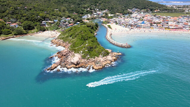 Panoramic aerial view of Barra da Lagoa Beach in Florian&oacute;polis Santa Catarina Brazil with yacht sailing in turquoise blue sea on a sunny summer day with the beach crowded with people.
