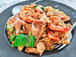 Pad See Ew Delight: A close-up of Pad See Ew, a popular street food, offering a flavorful combination of stir-fried noodles, succulent shrimp, squid and vegetables.