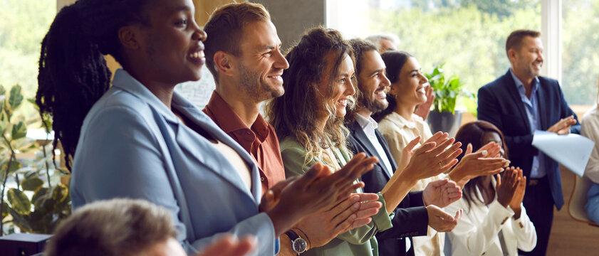 Happy diverse audience applauding after speaker finishes successful presentation at public business conference. Group of multiethnic people standing in row, clapping hands and smiling. Banner, header